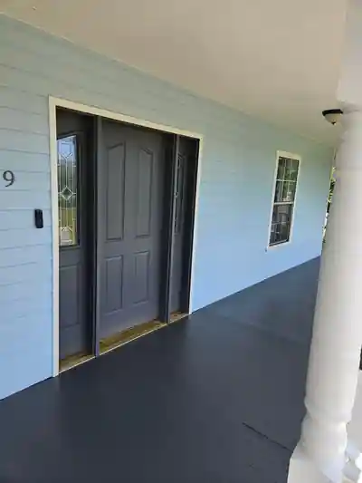 Charcoal front door and white-railed porch of the blue farmhouse