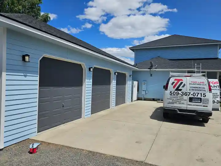 A blue detached garage with charcoal doors and the white Top Line van parked in front