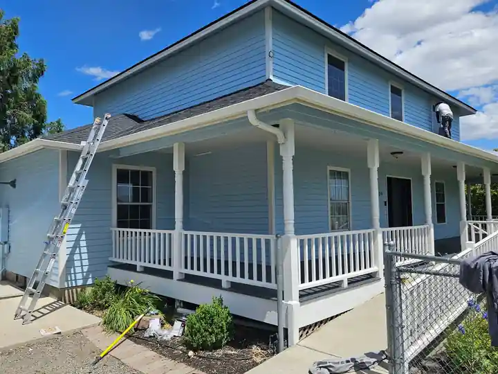 Front porch of the blue farmhouse: white columns and railing, charcoal door, a ladder still leaning on the porch