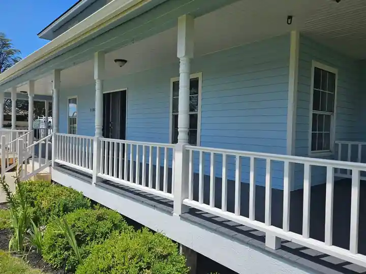Detail of the white wraparound porch railing on a freshly painted blue farmhouse