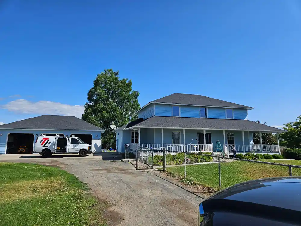A pale blue two-storey farmhouse with a white wraparound porch and a matching detached garage, freshly painted by Top Line, with the company van parked by the garage