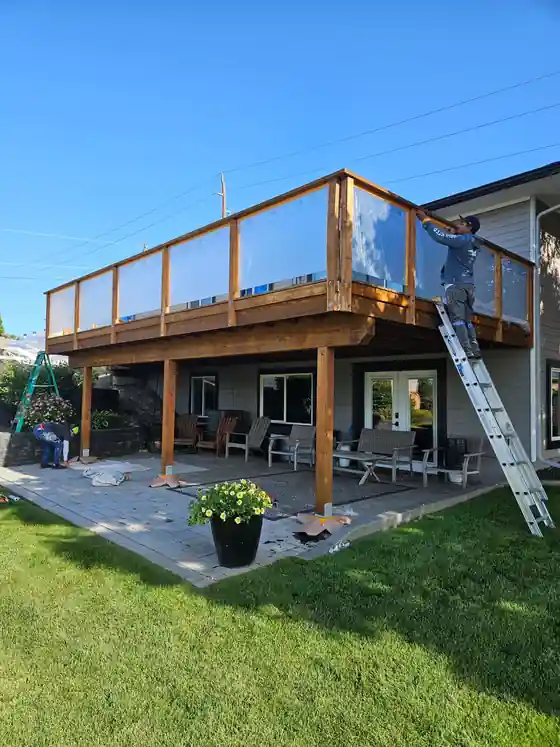 An elevated deck with a glass railing and a crew member on a ladder beside it