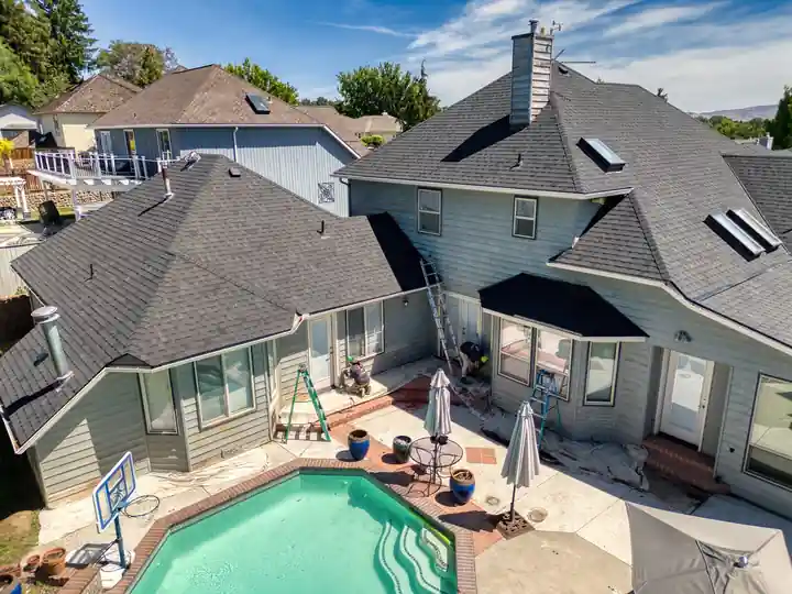 Aerial view of a grey pool home from the back, ladders up against the rear wall during an exterior repaint