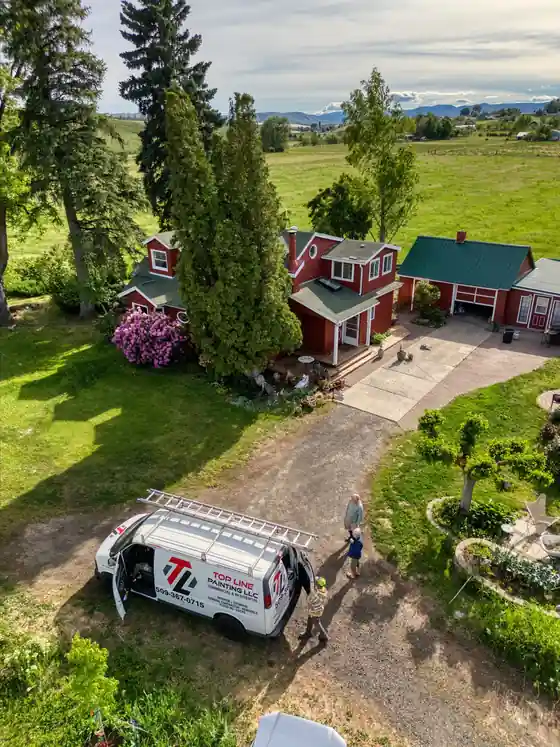 Aerial view of a red farmhouse with green roofs among fields, the Top Line van with its ladder rack in the drive