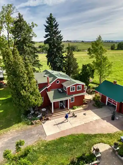 Aerial view of a red farmhouse up close, with crew members on the porch