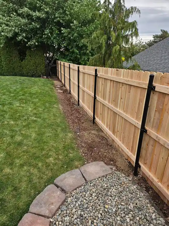 A cedar fence line on black steel posts above a river-rock bed
