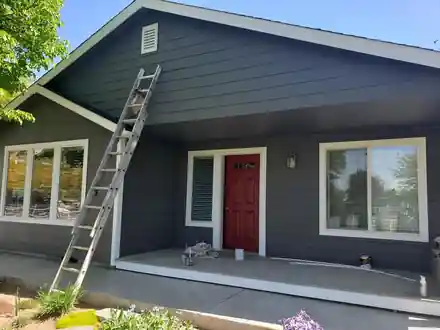 A charcoal ranch house with white trim, a red front door and a ladder still standing against it