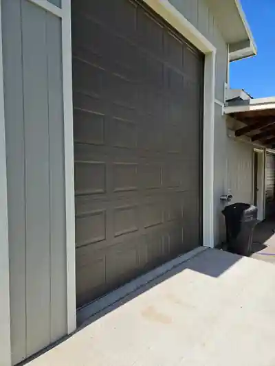 A dark brown garage door set in grey siding