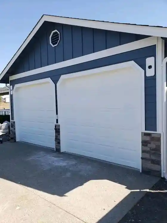 A navy board-and-batten garage with white doors, a Top Line paint job