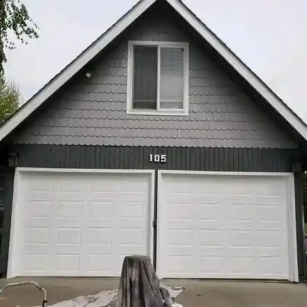 A grey shingle gable above white garage doors, with a drop cloth still down