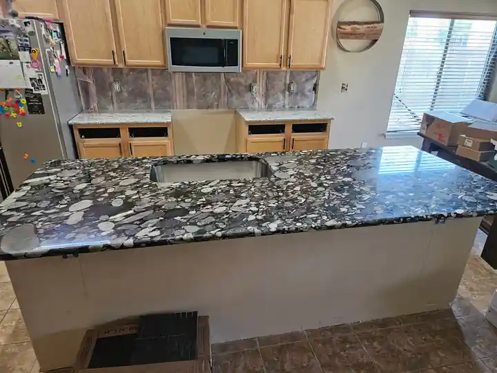 A kitchen remodel by Top Line: a new granite countertop on the island, light maple cabinets beyond