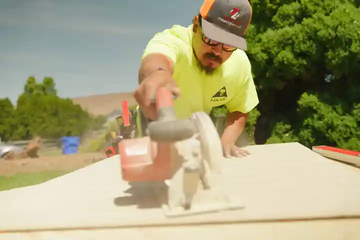 A Top Line crew member in a hi-vis shirt cutting a board with a circular saw