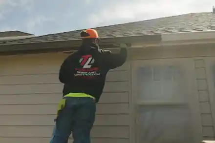 A painter on a ladder painting the eaves, wearing a Top Line hoodie