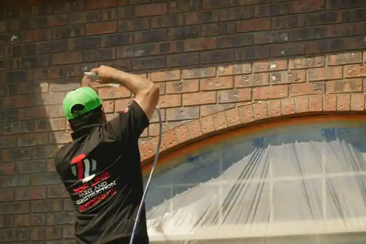 A Top Line painter spraying a brick archway with the neighboring window masked off
